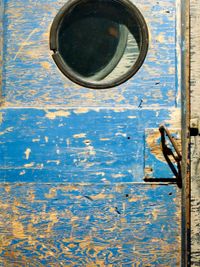 A close-up orthogonal view of the worn-out wooden door, handle, and window of an old snowmobile.