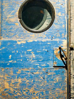 A close-up orthogonal view of the worn-out wooden door, handle, and window of an old snowmobile.