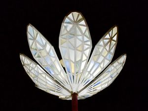 An outdoor art installation in the shape of a flower is lit up at night against a pitch black sky.