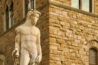 A nude statue of Neptune stands alone at the corner of an old brown stone building.