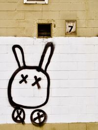 An orthogonal view of a brown and white concrete wall. There is a parking sign with the number '7' on it and graffiti of a simiplied rabbit with Xs for its eyes.
