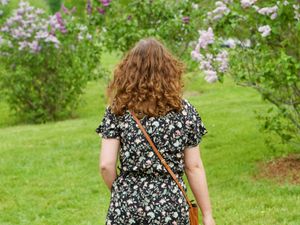 A woman walks away from the camera towards a field of lilacs in bloom.