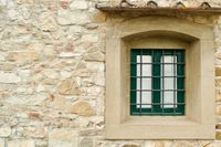 An orthogonal view of an old stone wall with a green window behind metal bars.