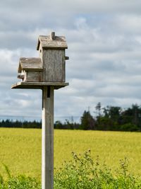 A two-storey birdhouse sits on a post in front of a farmer's field.