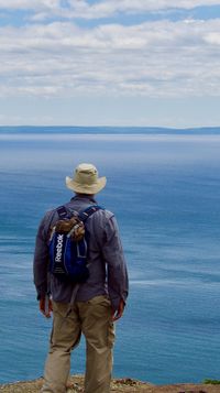 A man in hiking clothes stands in the foreground with his back to the camera as he looks out over Lake Superior.