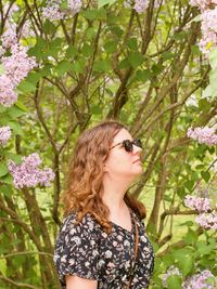Side profile of a pretty woman standing quietly with her head and shoulders framed by pink lilac blossoms.