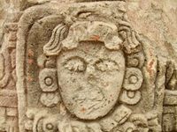 Close-up of a Mayan face carved in stone and mostly worn away over centuries.