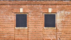 An orthogonal view of an old brick wall with two windows filled in with black bricks.