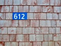 An orthogonal view of a worn wall that use to be red. The newest part of the wall is a bright blue sign that reads, '612'.