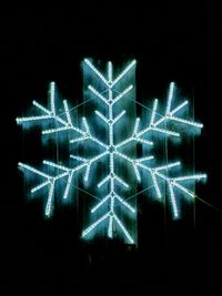 A blue neon snowflake hangs on an old barn wall at night.