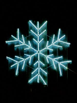 A blue neon snowflake hangs on an old barn wall at night.