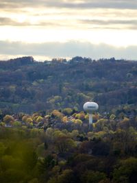 A view of a round white water tower surrounded by rolling hills, trees, and the rooftops of some local homes.