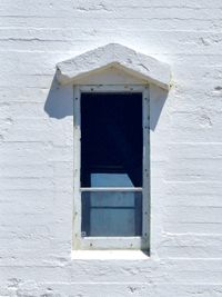 A minimalist, orthogonal view of a simple lighthouse window on a white wall. The window has a very small arched canopy that resembles an upward arrow.