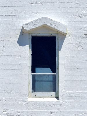 A minimalist, orthogonal view of a simple lighthouse window on a white wall. The window has a very small arched canopy that resembles an upward arrow.
