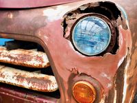 Close up of the rusted front grill and headlight of a very old pickup truck.