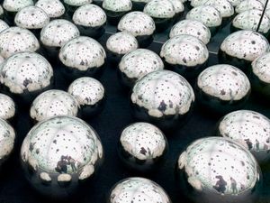 An art installation made up of dozens of smooth mirrored spheres in different sizes, each one reflecting its neighbors. The photographer and other people can be seen in the reflections of several spheres.