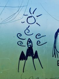 A close-up shot of mountains and wind drawn in black permanent marker on a foggy window. The outside is so blurred it forms a soft top-to-bottom gradient from blue to green.