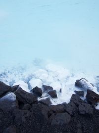 Looking down at rough lava rocks against the blue/turquoise water of a hot spring. Where the water and rocks meet it's foamy and bubbly.