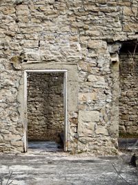 The ruins of an old mill. A rough stone wall with open doorways can be seen with vines crawling across it.