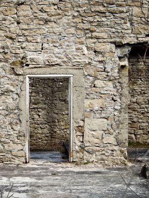 The ruins of an old mill. A rough stone wall with open doorways can be seen with vines crawling across it.