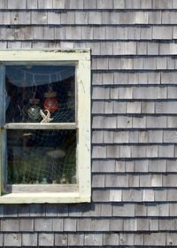An orthogonal view of an old fishing shack, with various pieces of fishing equipment hanging in a window.