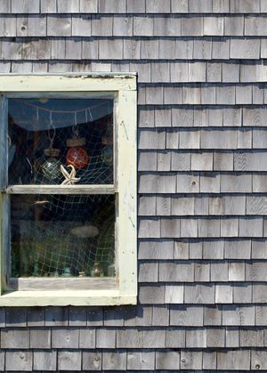 An orthogonal view of an old fishing shack, with various pieces of fishing equipment hanging in a window.