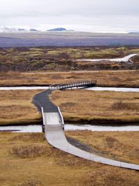 A pathway and some bridges meander into the distance in this landscape shot. Lava fields stretch out to the horizon where snow-covered mountains can be seen.