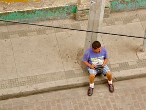 Candid street scene looking down at a man sitting on the sidewalk holding an FM radio.