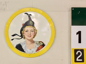 An abstract of a wall at a curling rink, featuring part of a scoreboard and a framed vintage painting of a woman in Scottish dress.