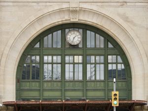 Street level view of the green archway and windows above the main entrance to Winnipeg's train station. The analog clock shows 1:34pm in roman numerals.