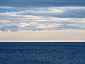 Numerous cloud banks coalesce over the horizon of a deep, dark blue Lake Huron.