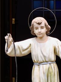 Funny shot of a weathered statue of Jesus as a child. His head is framed in a halo but his outstretched hand is holding a power cord with the plug dangling.