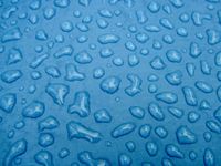 Closeup of the surface of a blue tent covered in undisturbed raindrops on various shapes and sizes.