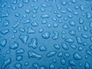 Closeup of the surface of a blue tent covered in undisturbed raindrops on various shapes and sizes.