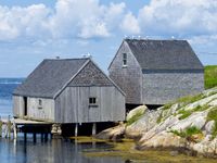 Two grey fishing shacks perched on the rocks overlooking Peggy's Cove, with seagulls resting on the rooftops.