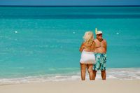 Candid shot of a man and woman standing together on the beach. The colors of their swimsuits complement those of the beach and water. Their tans do not.