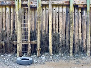 A weathered pier, the ocean floor, and a lone tire are exposed at low tide.